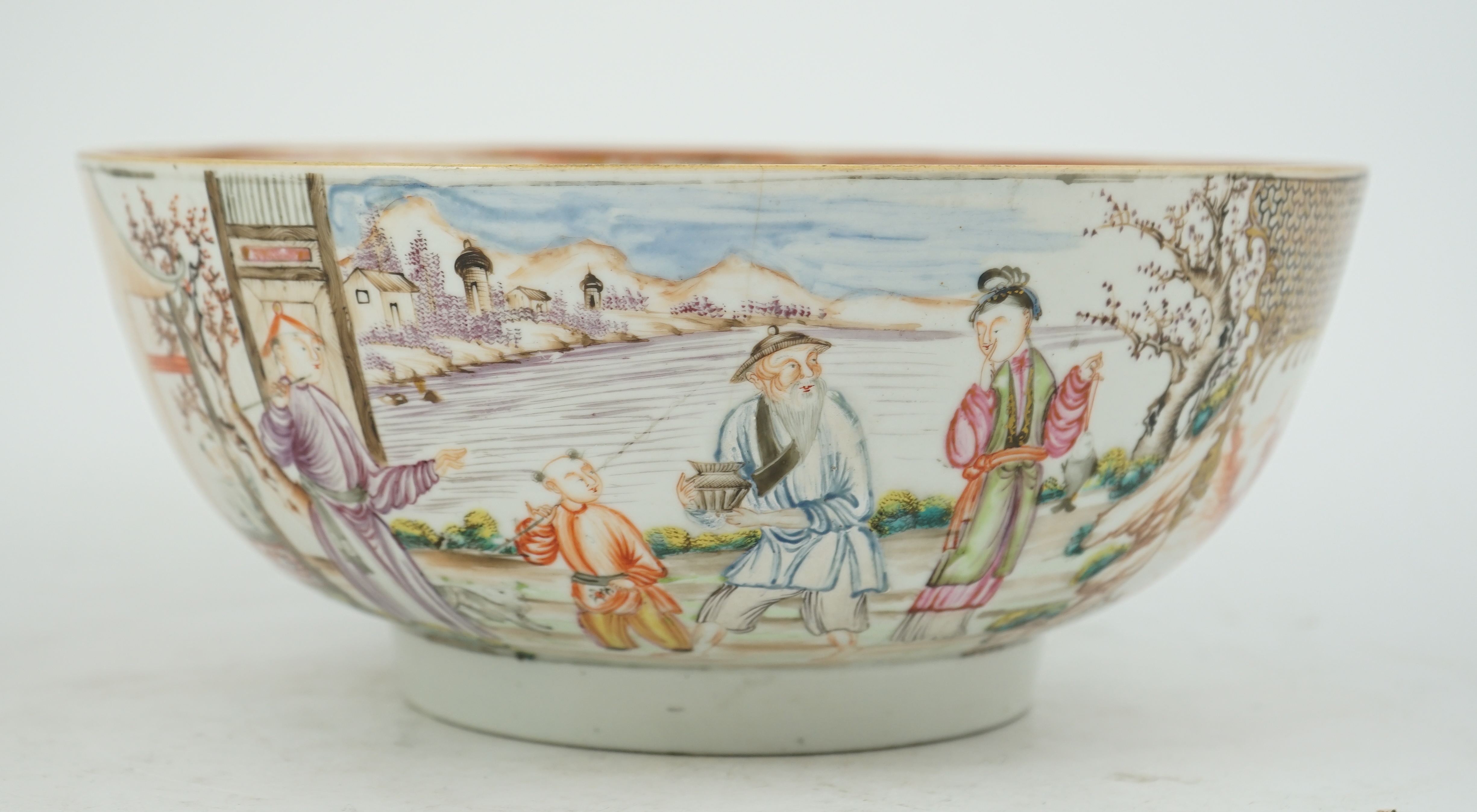 A Chinese famille rose ‘mandarin’ bowl, Qianlong period, painted with figures in a lakeside garden, between red enamelled landscape vignettes and cellular panels, 28.4cm diameter. Condition - there is a hairline crack to